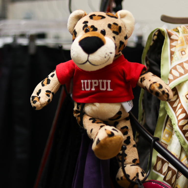The stuffed PAWS character on a rack of clothes.