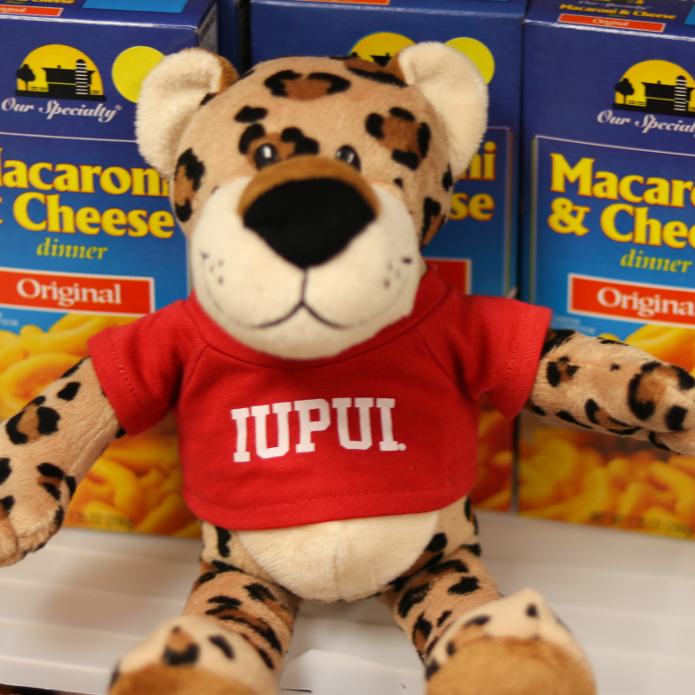 The PAWS stuffed character sitting with some macaroni and cheese.