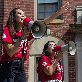 Two resident assistants with megaphones speak to their residents outside Ball Hall.