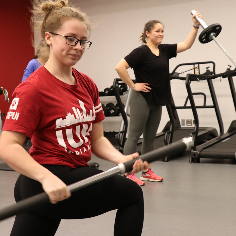Two female students work out in a gym.