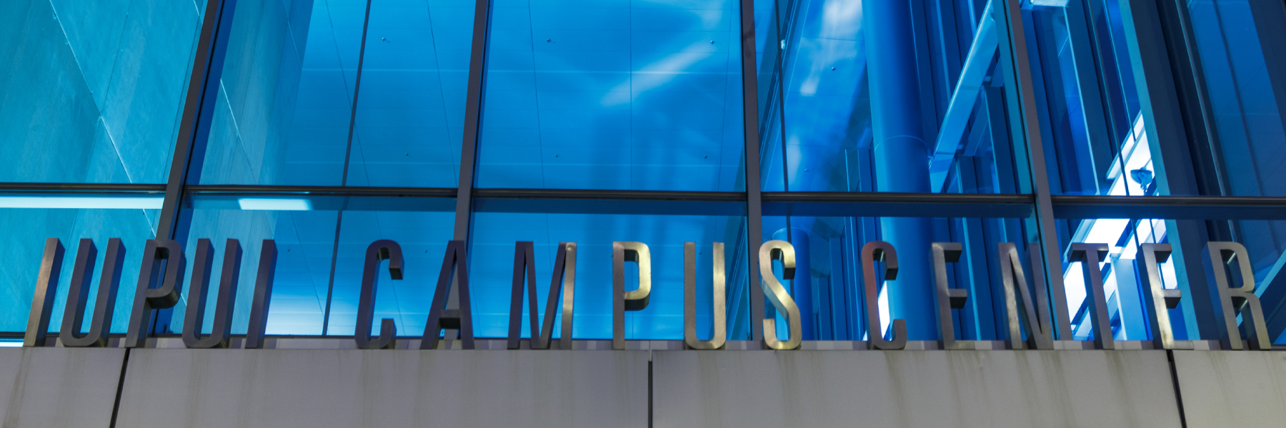 Night time photo of the campus center sign in front of the building over the doors that says IUPUI Campus Center.