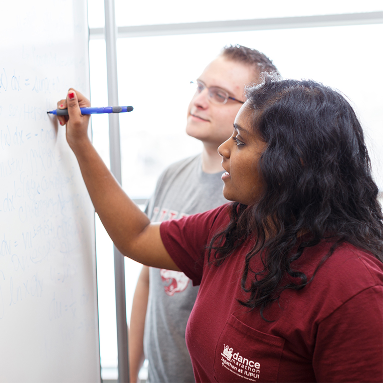 Two students write on a white board in the cube