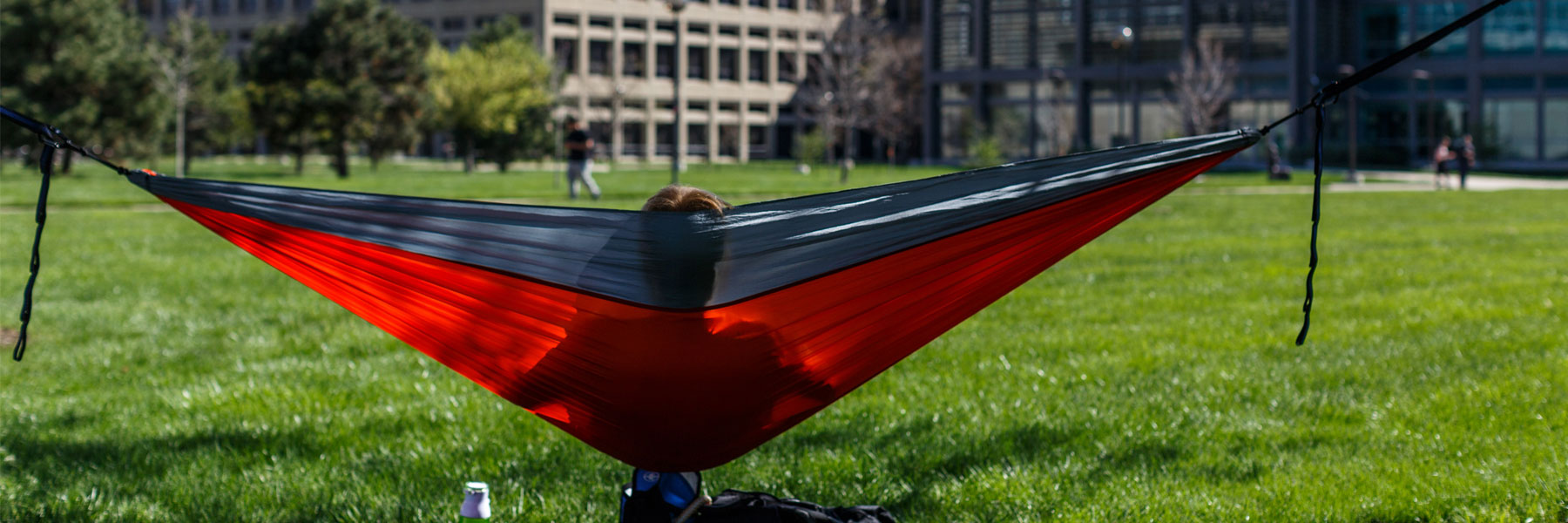 A student hanging out in a hammock on the lawn outside of University Library.