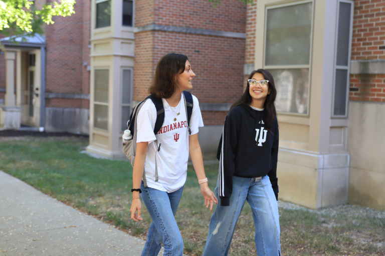 Two students walking on the sidewalk by the Riverwalk apartments.